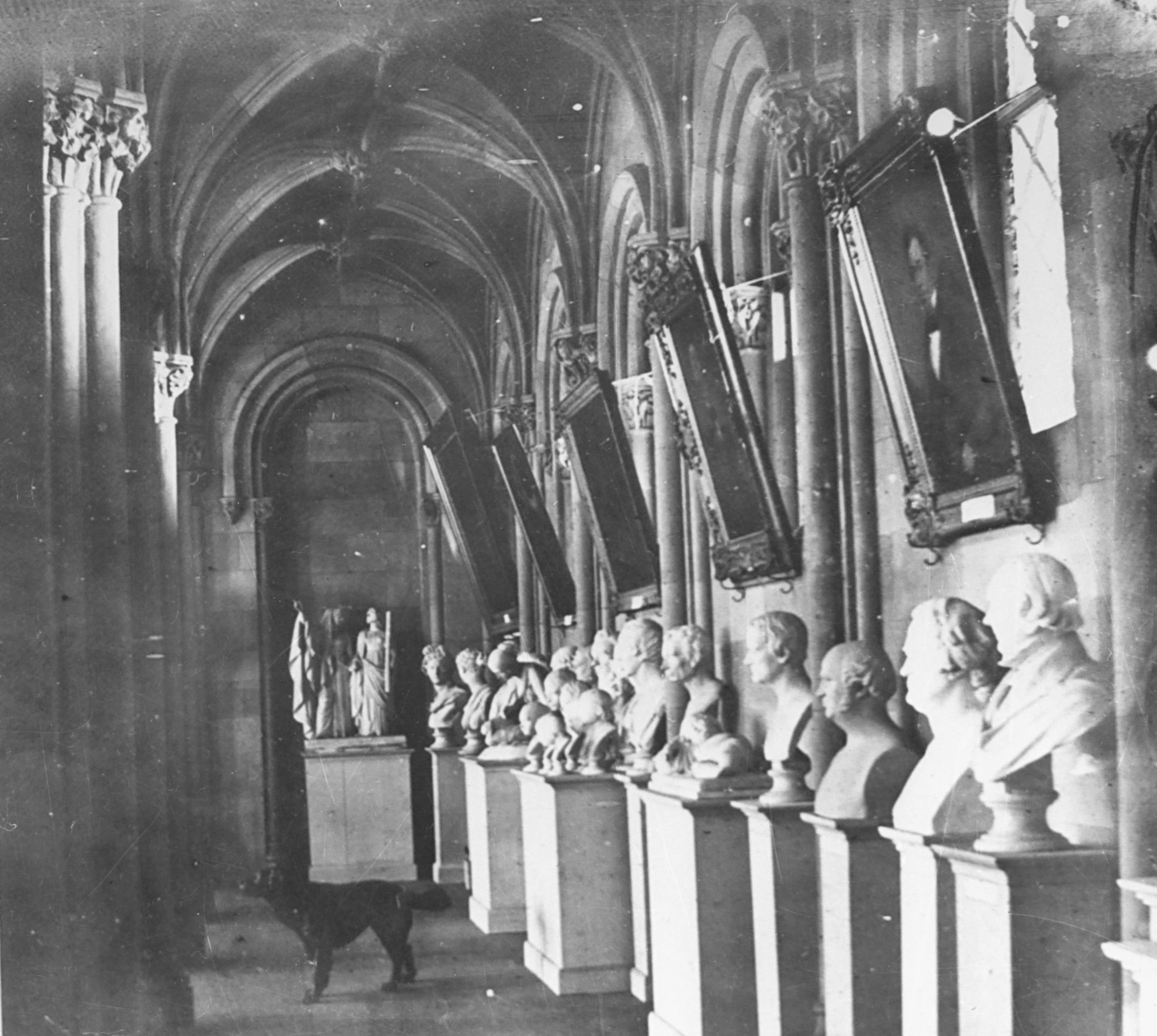 Interior image of the north-facing west range showing sculptures on pedestals lining the wall with hanging portraits.