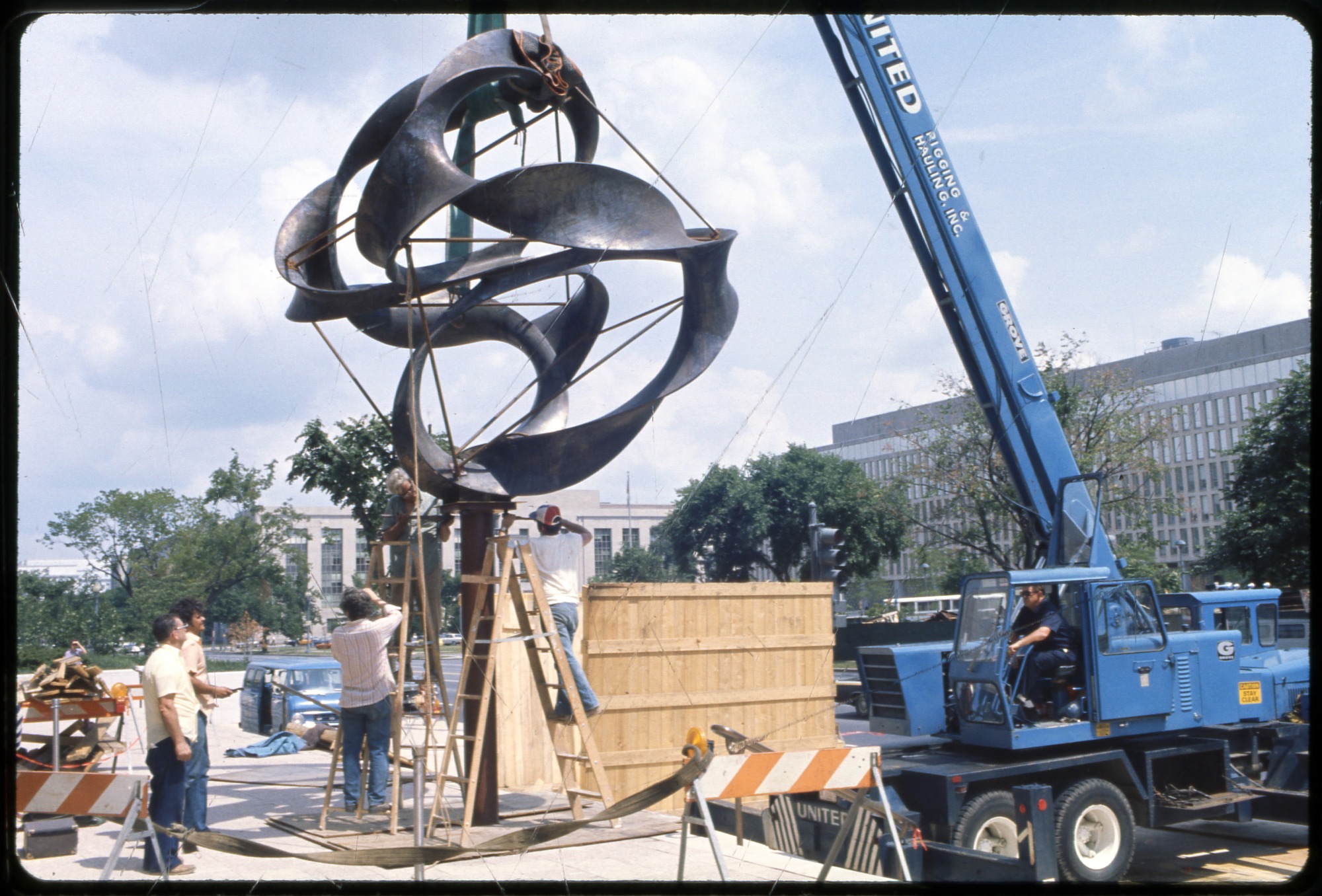 Crane lowering a spiral sculpture on a tall stone base.