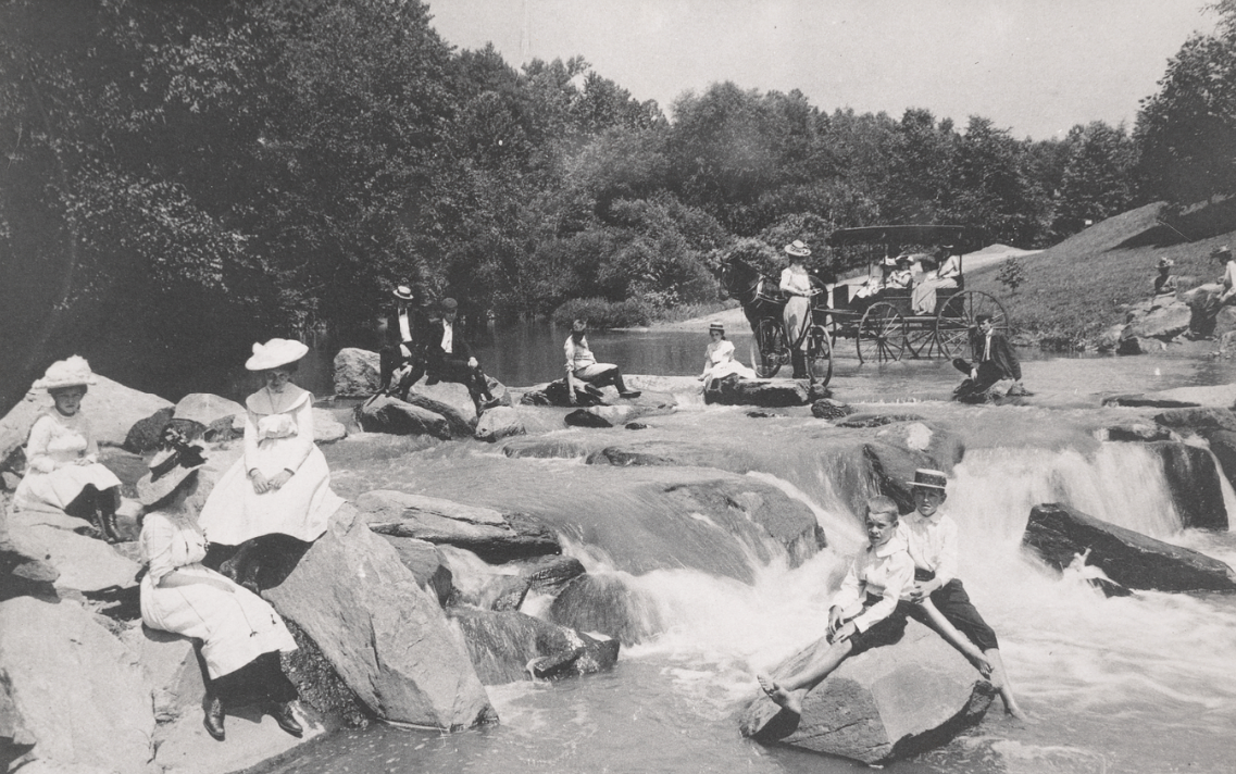 Black and white image of people sitting on rocks on a creek.