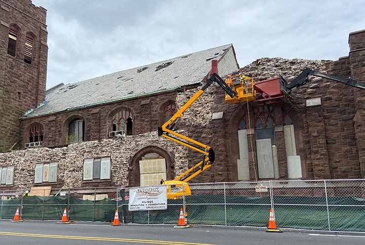 Image of two people wearing safety gear on a telehandler next to the exterior roof of the First Victory Presbyterian Church.