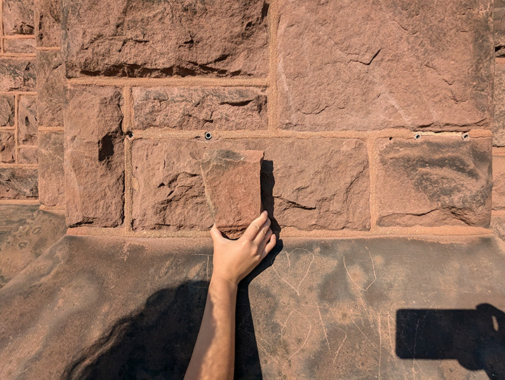 Image of a hand holding a piece of the Castle’s Seneca sandstone up against First Victory’s sandstone, 2024.