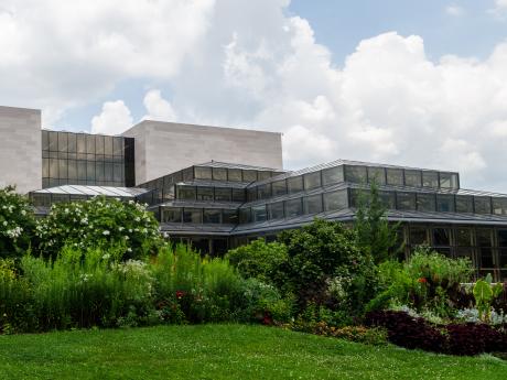 View of a glass addition to a stone building, with plantings and sky.